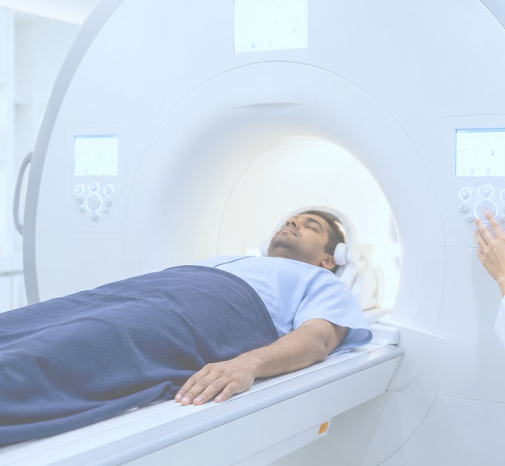 A patient lying on the MRI table with a head coil and headphones fitted, positioned at the mouth of the scanner bore.